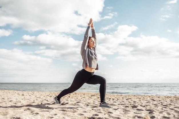 Aantrekkelijke fitte vrouw die yoga asana beoefent op het strand op een heldere zonnige dag Warrior 1 pose