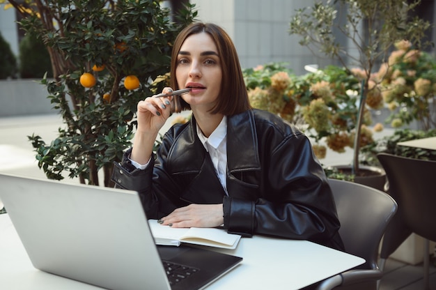 Aantrekkelijke freelance mooie vrouw, jonge zakenman, copywriter, camera kijken met behulp van laptop zittend aan tafel in een terras van cafetaria en op afstand werken. Online bedrijfsconcept