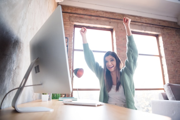 Aantrekkelijke gekke jonge vrouw die computer op tafel werkt, wint thuis vuisten