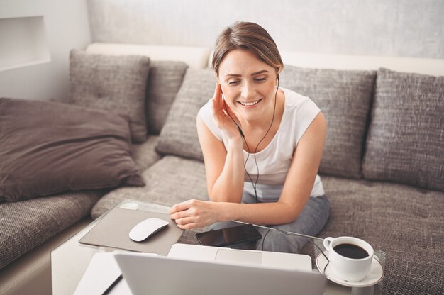 Aantrekkelijke gelukkige jonge student online studeren thuis, met behulp van laptopcomputer, hoofdtelefoons, met video-chat, zwaaien. Werken op afstand, onderwijs op afstand. Videoconferentie of virtueel evenement in quarantaine