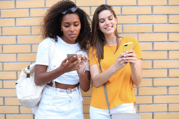 Aantrekkelijke gelukkige jonge vrouwen vrienden buitenshuis met behulp van mobiele telefoons chatten.