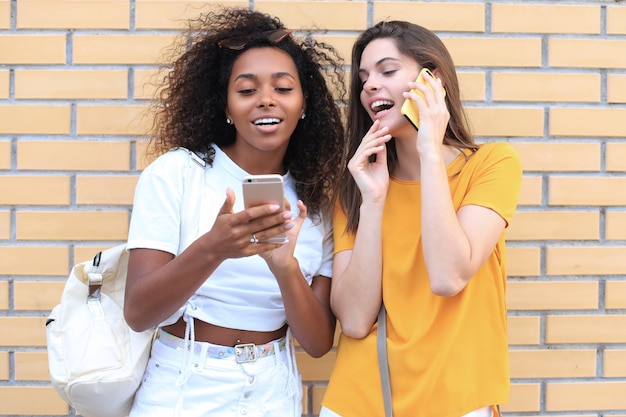 Aantrekkelijke gelukkige jonge vrouwen vrienden buitenshuis met behulp van mobiele telefoons chatten.