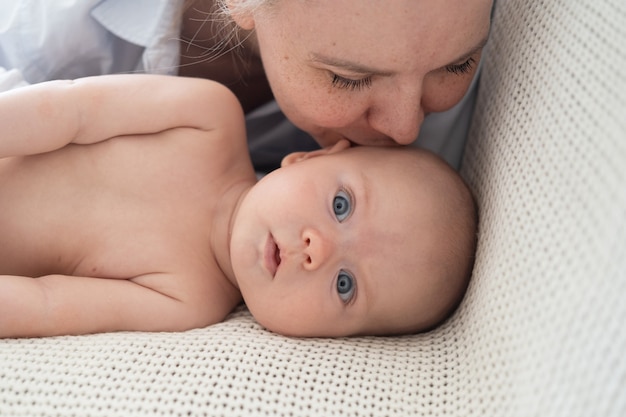 Aantrekkelijke gelukkige volwassen moederkus die met kleine babyjongen ligt. genietend moment thuis samen, zorgzame moeder. Kinderopvang, kraamconcept. Gelukkig gezin. Tederheid. Hoge kwaliteit foto