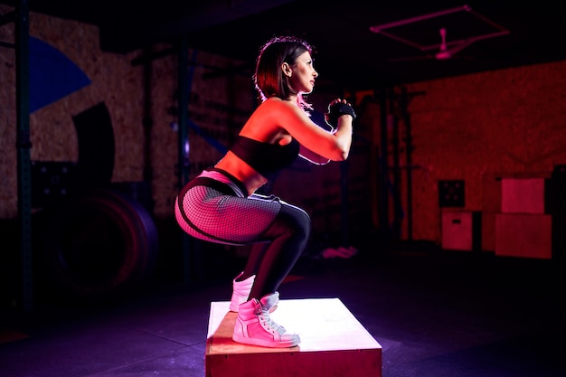 Aantrekkelijke geschikte middenleeftijdsvrouw die doos doen die bij een dwars geschikte stijl springen. De vrouwelijke atleet voert sprongen bij gymnastiek uit