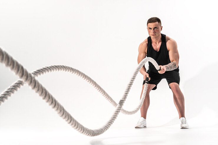 Aantrekkelijke gespierde man uit te werken met zware touwen. Foto van knappe man in sportkleding geïsoleerd op een witte muur. Crossfit