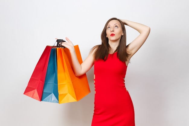 Aantrekkelijke glamour Kaukasische modieuze jonge bruinharige vrouw in rode jurk met multi gekleurde pakketten met aankopen na het winkelen geïsoleerd op een witte achtergrond. Kopieer ruimte voor advertentie.