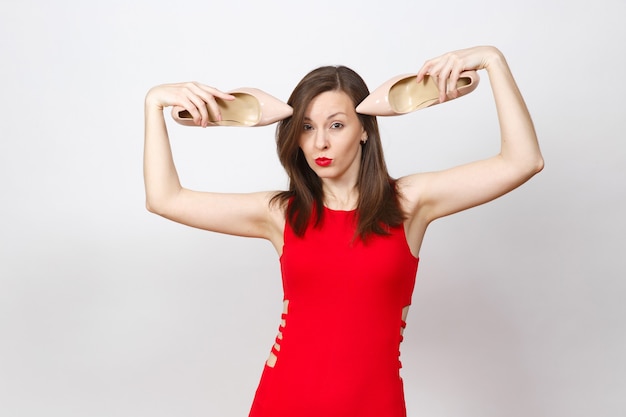 Aantrekkelijke glamour modieuze jonge bruinharige vrouw in rode jurk hakken op het hoofd, beige schoenen krijgen met rode zool van haar winkelen geïsoleerd op een witte achtergrond. Kopieer ruimte voor advertentie.