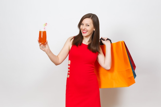 Aantrekkelijke glamour modieuze jonge vrouw in rode jurk met glas drankje cocktail, multi gekleurde pakketten met aankopen na het winkelen geïsoleerd op een witte achtergrond. Kopieer ruimte voor advertentie.