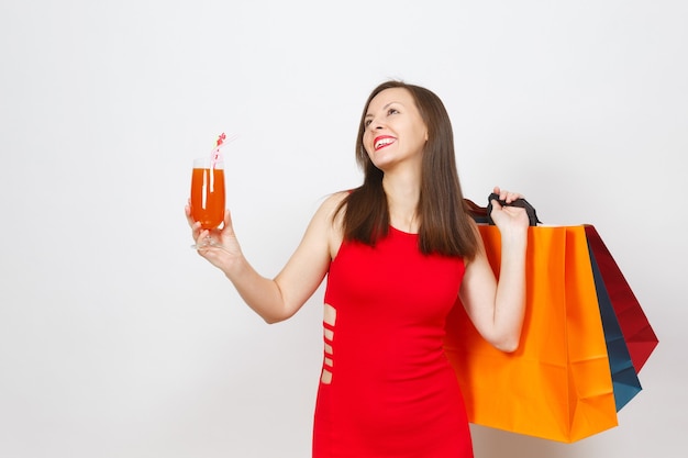 Aantrekkelijke glamour modieuze jonge vrouw in rode jurk met glas drankje cocktail, multi gekleurde pakketten met aankopen na het winkelen geïsoleerd op een witte achtergrond. Kopieer ruimte voor advertentie.