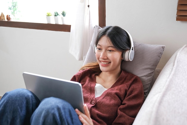 Aantrekkelijke glimlachende jonge vrouw die tablet gebruikt en muziek luistert op de bank thuis lifestyle concept