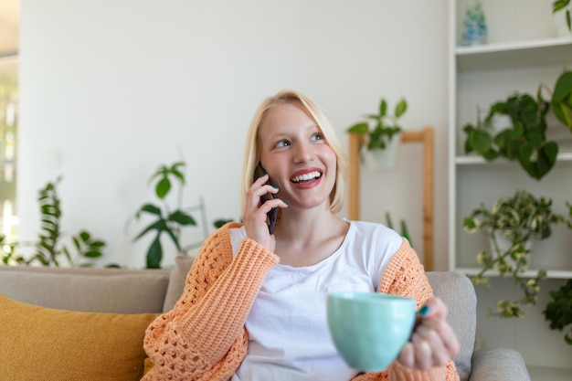 Aantrekkelijke glimlachende vrouw die smartphone gebruikt terwijl ze thuis op de bank zit Communicatie en gezelligheid concept