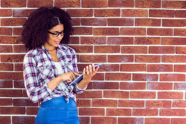 Aantrekkelijke hipster die op muur leunt en tablet gebruikt