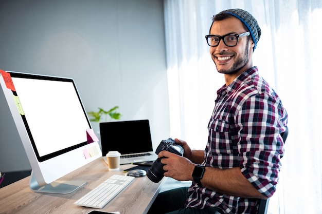 Aantrekkelijke hipster die terwijl het werken bij bureau glimlacht