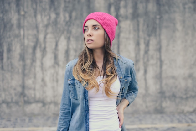Aantrekkelijke hipster meisje gekleed in wit t-shirt, jeans shirt en roze hoed poseren tegen grijze muur. Straatfoto's maken