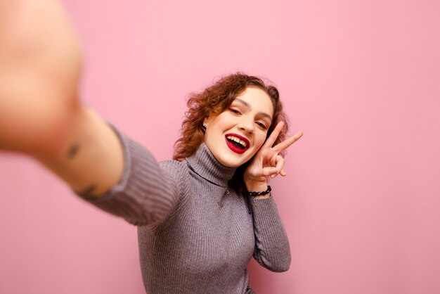 Aantrekkelijke hipster vrouw met make-up en krullend krullend haar neemt een selfie