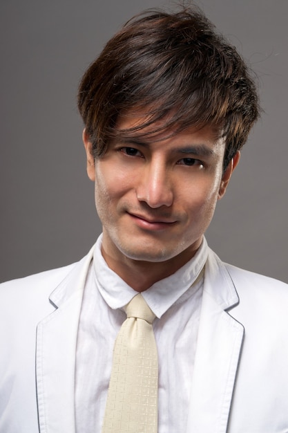 Aantrekkelijke jonge Aziatische man in wit pak, close-up portret op studio grijze achtergrond.