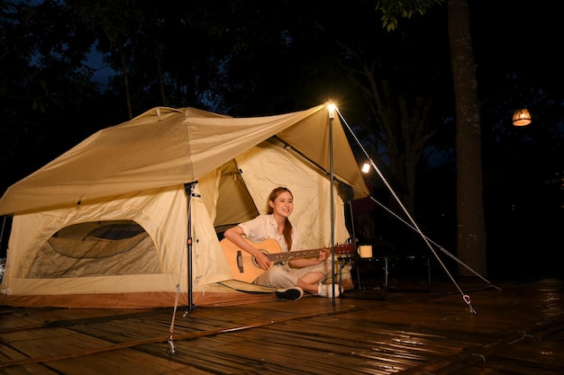 Aantrekkelijke jonge Aziatische vrouw die 's nachts gitaar speelt op de camping