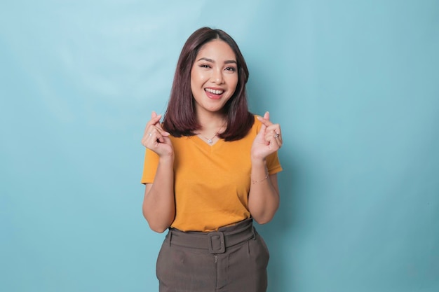 Aantrekkelijke jonge Aziatische vrouw voelt zich gelukkig en romantisch vormen hart gebaar drukt tedere gevoelens uit draagt casual gele t-shirt tegen blauwe achtergrond Mensen genegenheid en zorgconcept