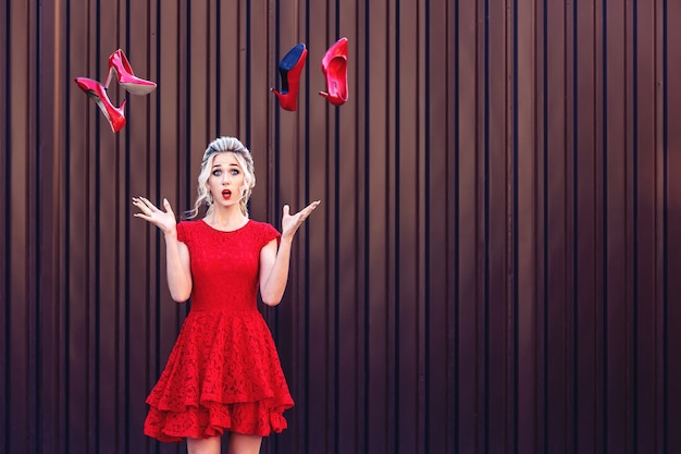 Aantrekkelijke jonge blonde in een rode jurk werpt rode schoenen op. Het concept van winkelen en verkopen