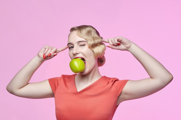 Aantrekkelijke jonge blonde met een retro kapsel heeft een groene appel in haar tanden