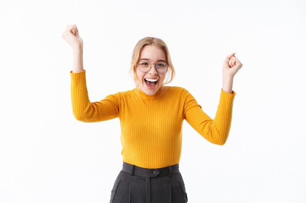 Aantrekkelijke jonge blonde vrouw die een trui draagt die over een witte muur staat en succes viert