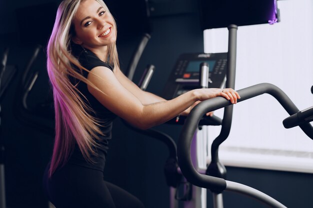 Aantrekkelijke jonge blonde vrouw die op cardio-trainingsapparatuur uitoefent