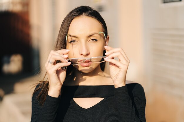 Aantrekkelijke jonge brunette vrouw draagt een zwarte top en een transparante bril die zich voordeed op straat.