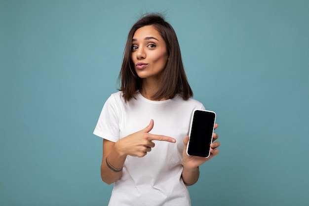 Aantrekkelijke jonge donkerbruine vrouw die er goed uitziet in een witte t-shirt die op een blauwe achtergrond staat?