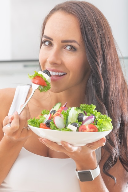 Aantrekkelijke jonge en gelukkige vrouw die groentesalade eet.