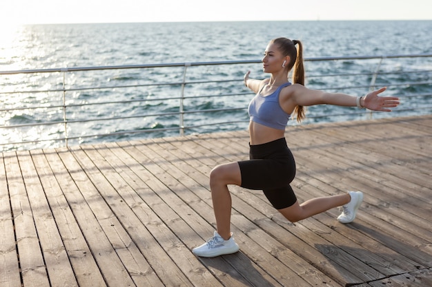 Aantrekkelijke jonge fitnessvrouw die hatha yoga-oefening beoefent bij zonsopgang op het strand