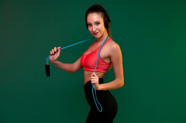 Aantrekkelijke jonge fitte vrouw met springtouw en koptelefoon binnenshuis doet aan lichaamsbeweging