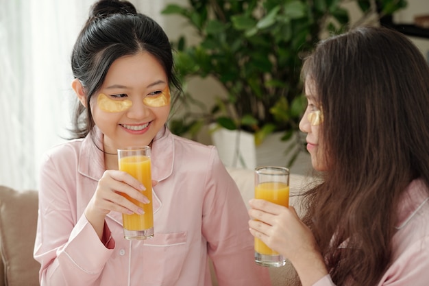 Aantrekkelijke jonge glimlachende vrouw met vlekken onder de ogen die een glas sap drinkt wanneer ze thuis tijd doorbrengt met haar beste vriend