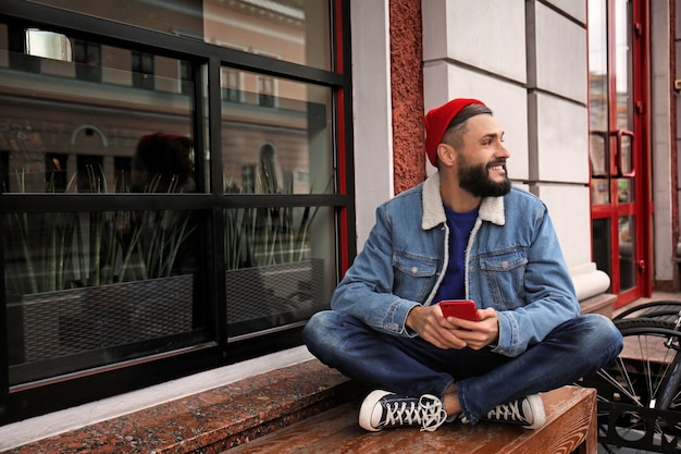 Aantrekkelijke jonge hipster met smartphone op straat in de stad