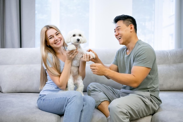 Aantrekkelijke jonge man en vrouw zitten op de bank en glimlachen. Ze aaien liefdevol het schoothondje