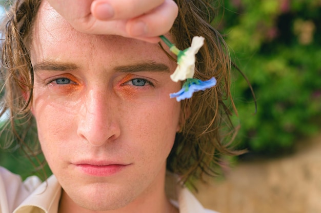 Aantrekkelijke jonge man met make-up poseert met bloemen die naar de camera kijkt