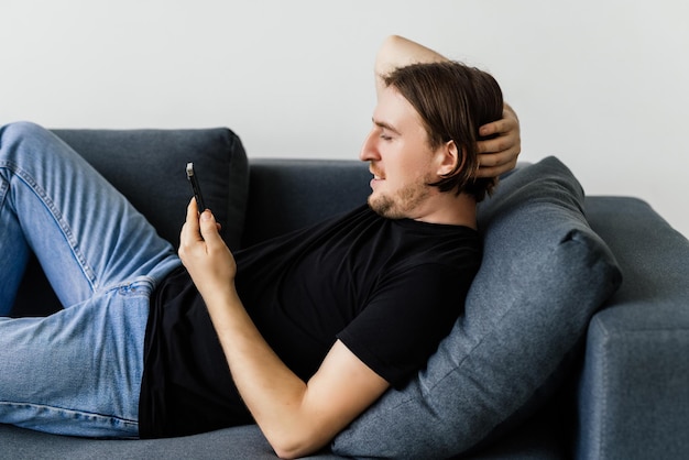 Aantrekkelijke jonge man zittend op een vloer in de woonkamer met behulp van mobiele telefoon