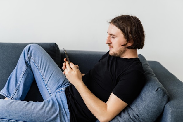 Aantrekkelijke jonge man zittend op een vloer in de woonkamer met behulp van mobiele telefoon