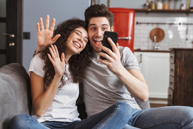 aantrekkelijke jonge paar man en vrouw die thuis op de bank zitten en samen selfie foto maken op smartphone