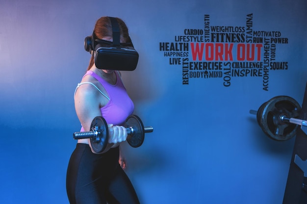 Aantrekkelijke jonge roodharige sportvrouw die biceps traint in de sportschool met VR futuristische bril.