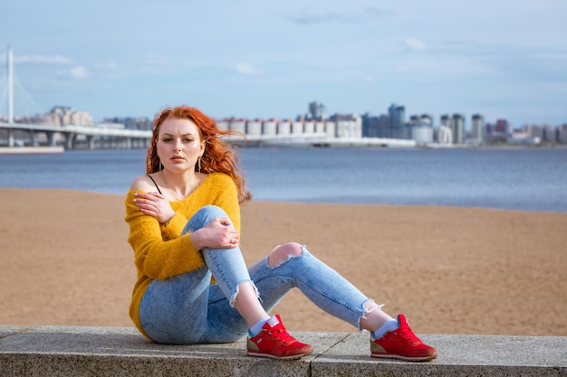 Aantrekkelijke jonge roodharige vrouw die buiten aan de waterkant zit en geel draagt