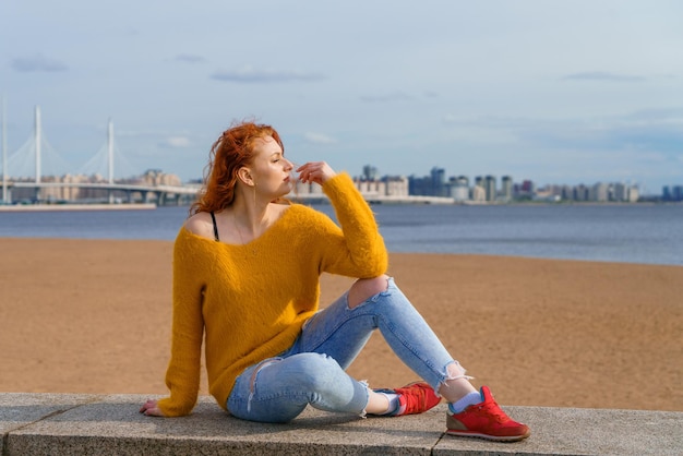 Aantrekkelijke jonge roodharige vrouw die buiten aan de waterkant zit en geel draagt