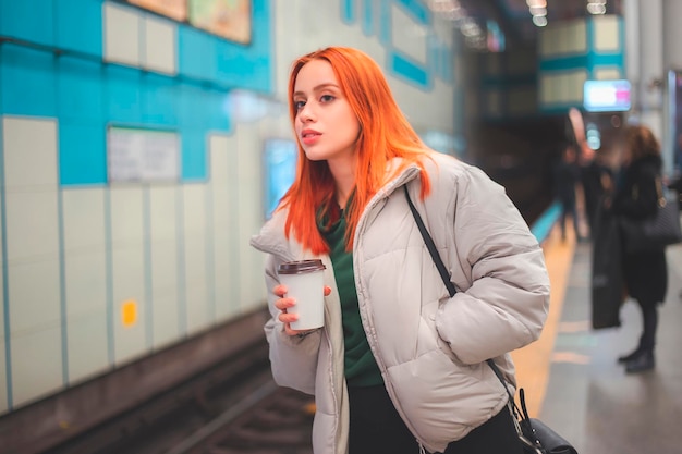 Aantrekkelijke jonge roodharige vrouw die wacht en op zoek is naar een volgende trein in een metrostation