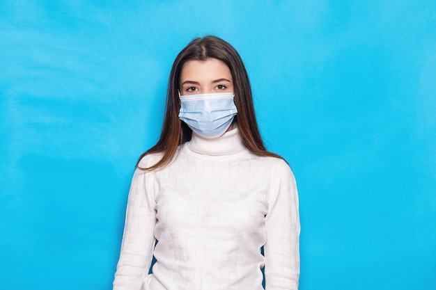 Aantrekkelijke jonge vrouw 20s in gezichtsmasker veilig voor coronavirus virus covid-19 tijdens pandemische quarantaine hand in hand gekruist geïsoleerd op heldere blauwe kleur achtergrond studio portret