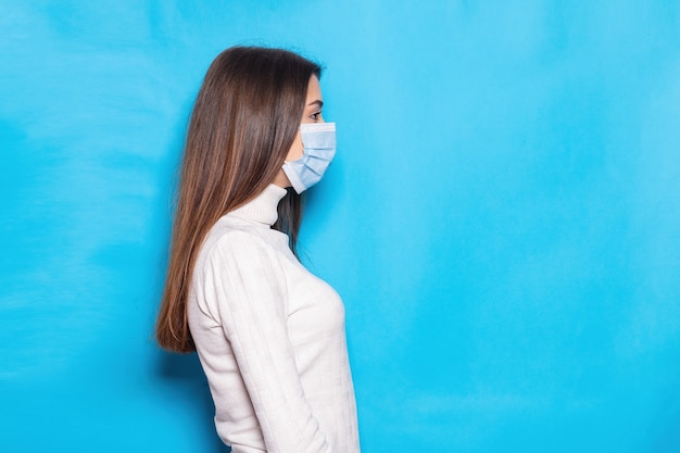 Aantrekkelijke jonge vrouw 20s in gezichtsmasker veilig voor coronavirus virus covid-19 tijdens pandemische quarantaine hand in hand gekruist geïsoleerd op heldere blauwe kleur achtergrond studio portret