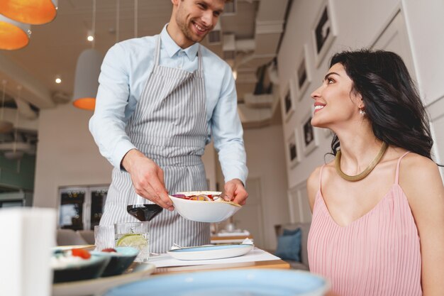 Aantrekkelijke jonge vrouw die naar cafémedewerker kijkt en glimlacht terwijl de man een bord heerlijke salade vasthoudt