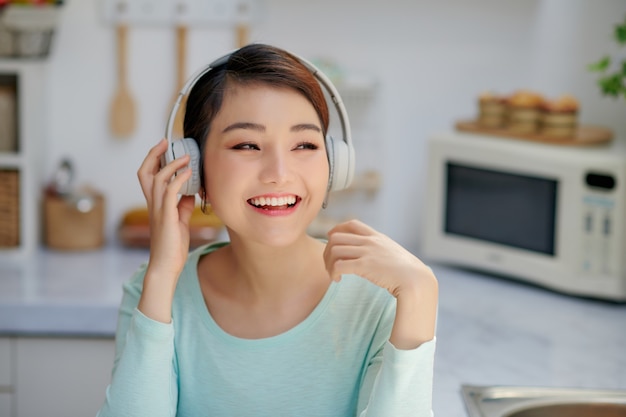 Aantrekkelijke jonge vrouw die naar muziek luistert met mobiele telefoon en koptelefoon tijdens het ontbijt in de keuken