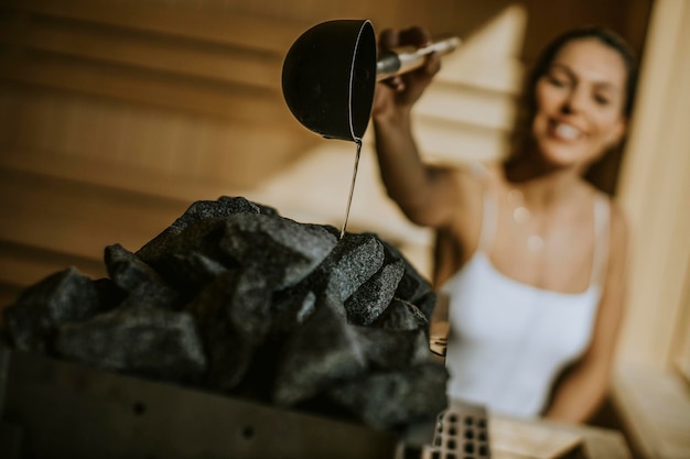 Aantrekkelijke jonge vrouw die water op hete steen in de sauna giet