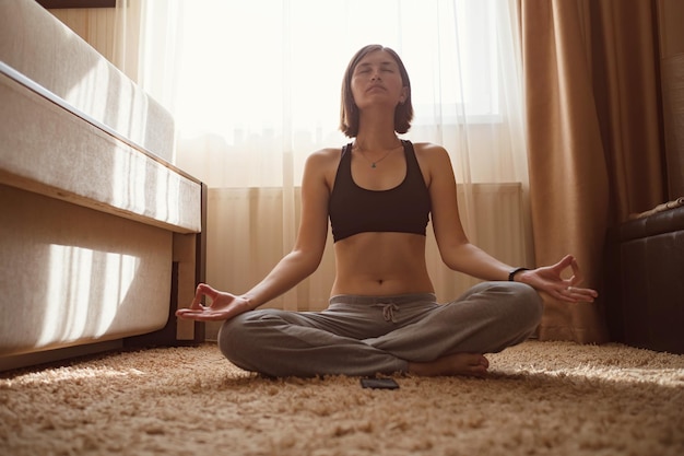 Aantrekkelijke jonge vrouw die yoga doet die yoga thuis online uitrekt