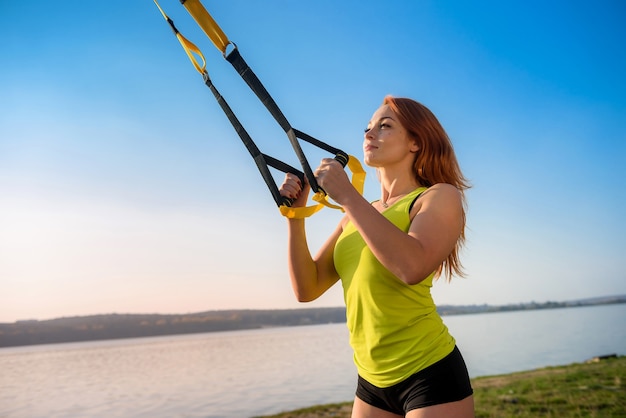 Aantrekkelijke jonge vrouw doet TRX training buiten in de buurt van het meer overdag. Gezonde levensstijl