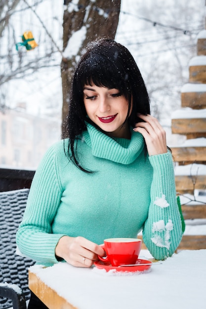 Aantrekkelijke jonge vrouw drinkt een kopje koffie in het straatcafé op een besneeuwde winterdag